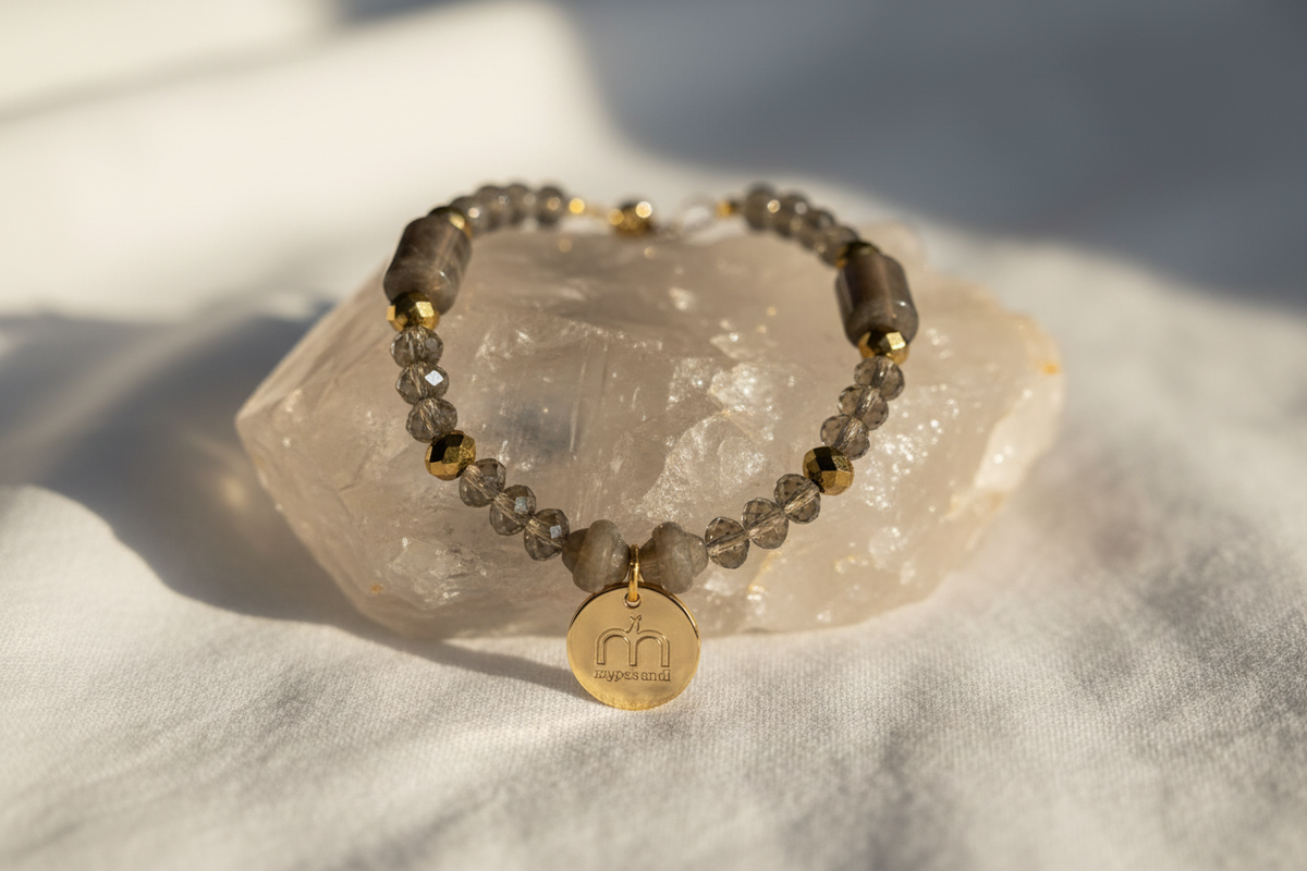 Collana Smoky Glow con cristalli sfaccettati fumé, dettagli oro e ciondolo logo dorato fotografata su un cristallo di quarzo – My Pets and I Milano