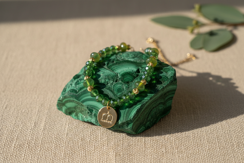 Collana Emerald Glow con cristalli sfaccettati verdi, dettagli oro e ciondolo logo dorato fotografata su una pietra di malachite – My Pets and I Milano