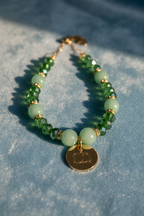 Collana Green Glow con pietre dure verdi, cristalli sfaccettati e ciondolo logo dorato fotografata su tessuto in velluto azzurro – My Pets and I Milano