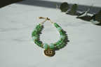 Collana Green Glow con pietre dure verdi, cristalli sfaccettati e ciondolo logo dorato appoggiata su una superficie in marmo bianca – My Pets and I Milano