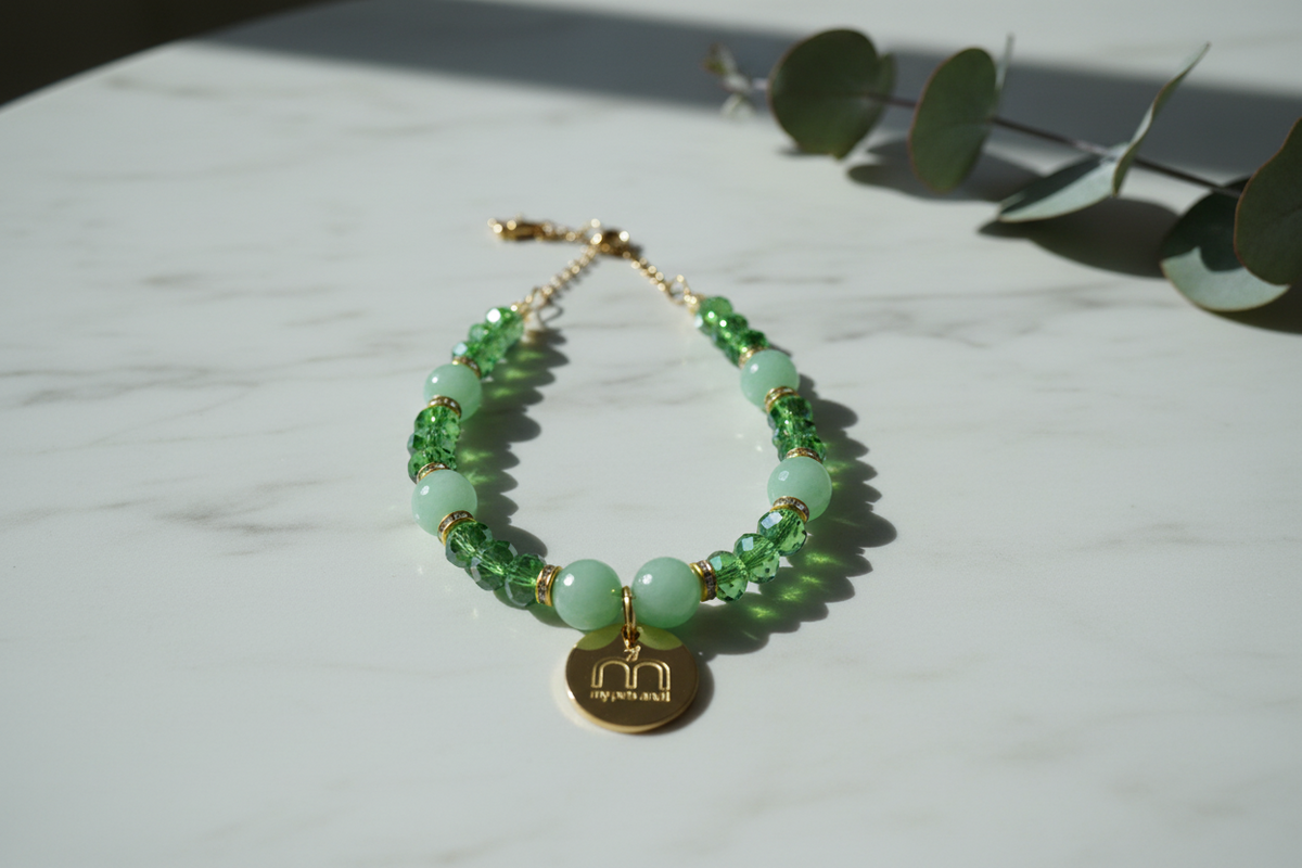 Collana Green Glow con pietre dure verdi, cristalli sfaccettati e ciondolo logo dorato appoggiata su una superficie in marmo bianca – My Pets and I Milano