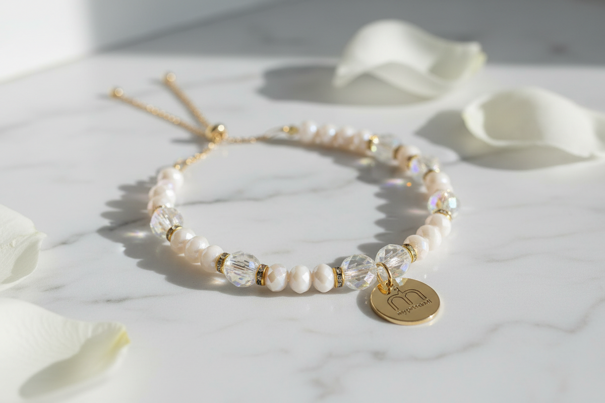 Collana Ivory Glow con cristalli sfaccettati avorio, cristalli trasparenti e ciondolo logo dorato fotografata su una superficie in marmo bianco con petali bianchi – My Pets and I Milano