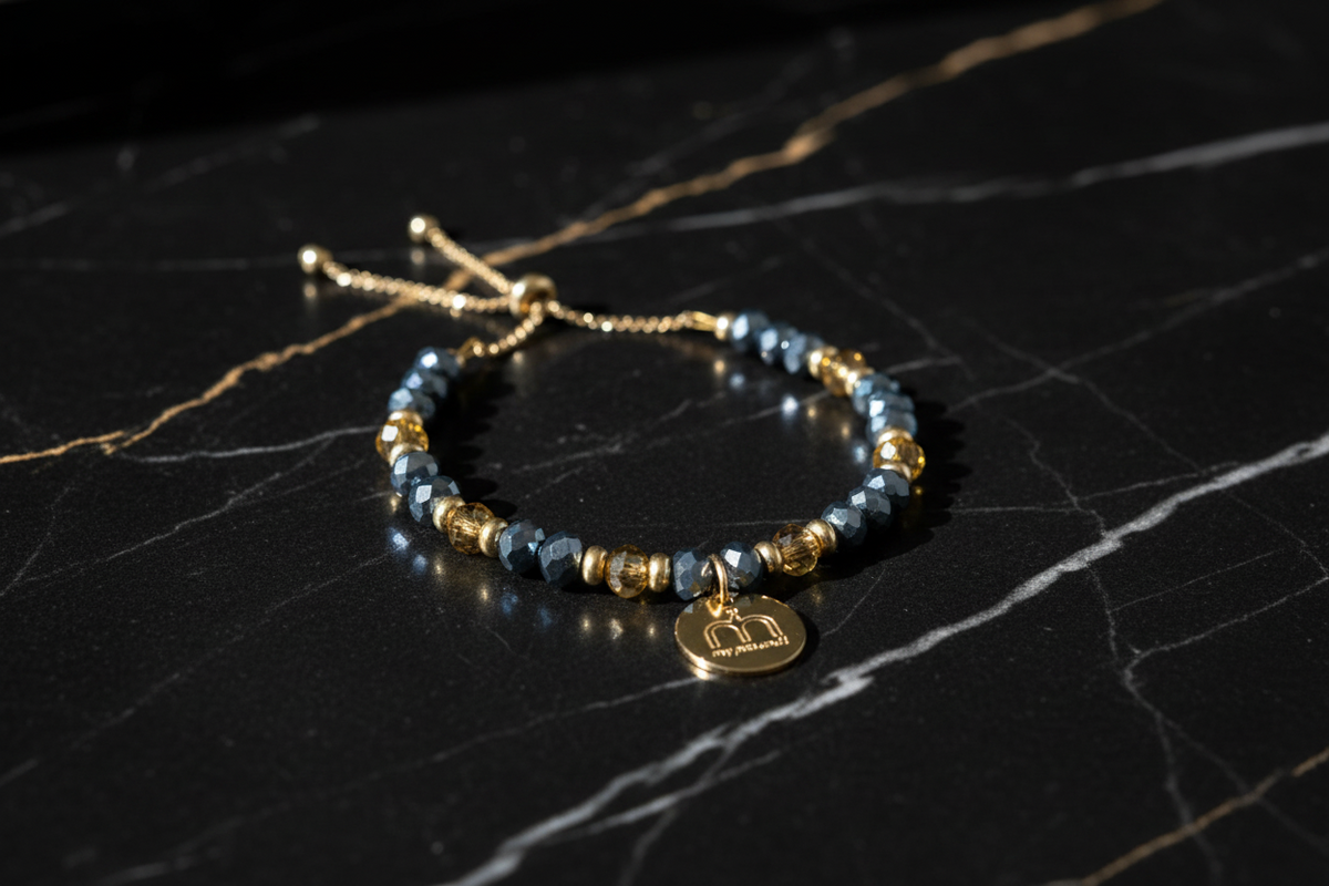 Collana Steel Glow con cristalli sfaccettati blu grigio, cristalli sfaccetat oro e ciondolo logo dorato fotografata su una superficie in marmo nero – My Pets and I Milano