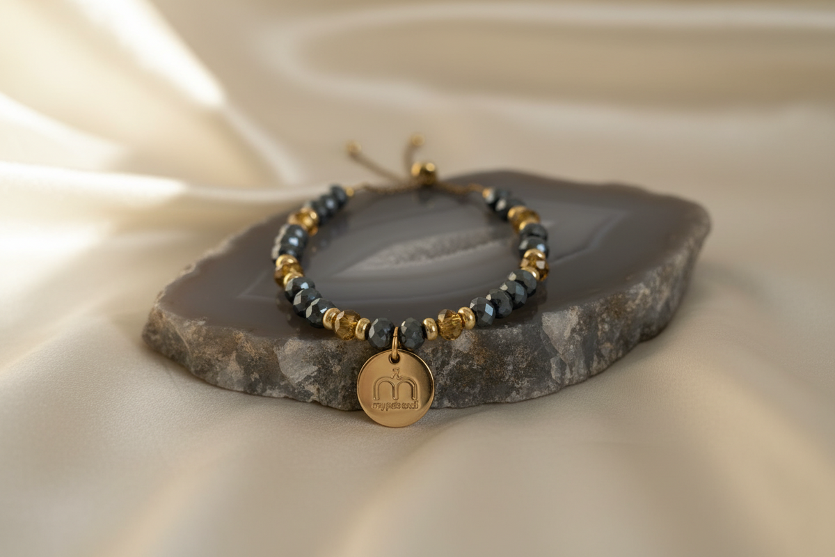 Collana Steel Glow con cristalli sfaccettati blu grigio, cristalli sfaccettati oro e ciondolo logo dorato fotografata su una base in agata grigia – My Pets and I Milano