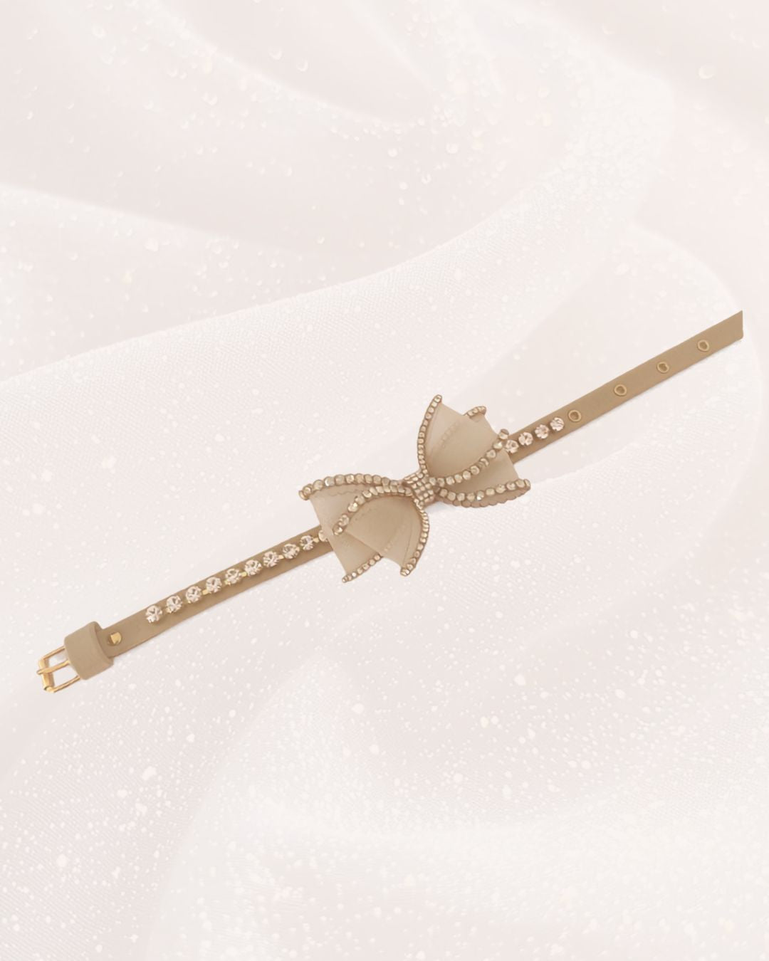 collare gioiello con fiocco strass e dettaglo colore oro appoggiato su tessuto bianco