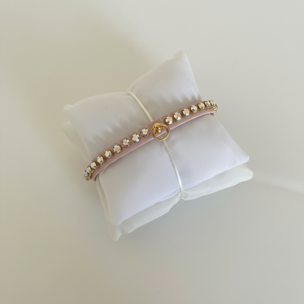 Collare rosa per cane con fila di strass sfaccettati e anello dorato, su cuscino bianco