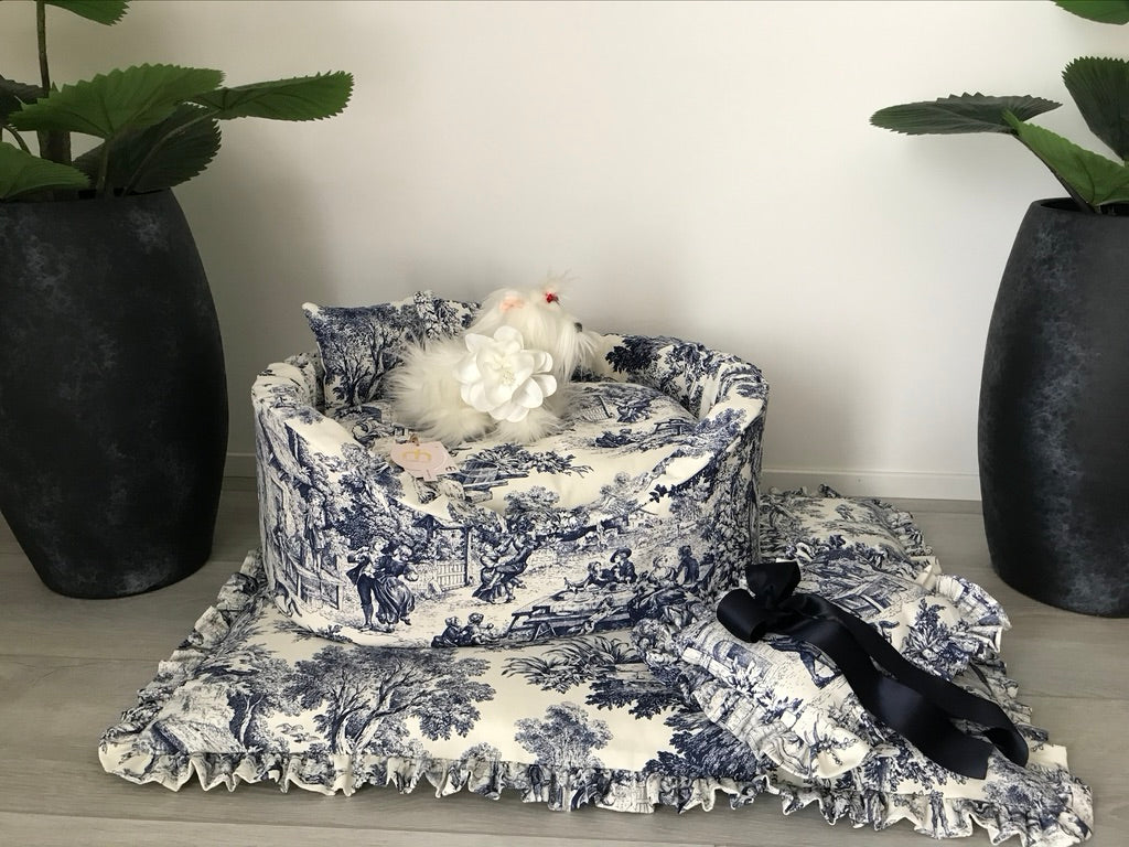 Cuccia sofà per cani in tessuto toile de jouy blu con materassino con rouche e cuscinetto coordinato appoggiati su pavimento.