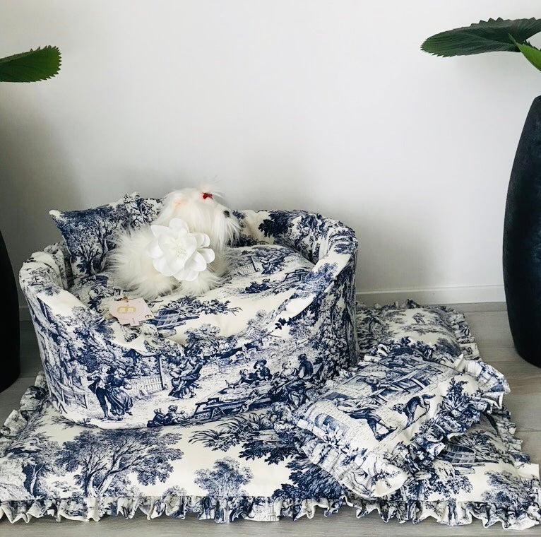 Cuccia sofà per cani in tessuto toile de jouy blu con materassino con rouche e cuscinetto coordinato appoggiati su pavimento.