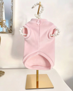 Vista posteriore della felpa in ciniglia rosa baby per cani con fiocchetto decorativo sul collo, esposta su supporto dorato con gruccia decorata da perle.