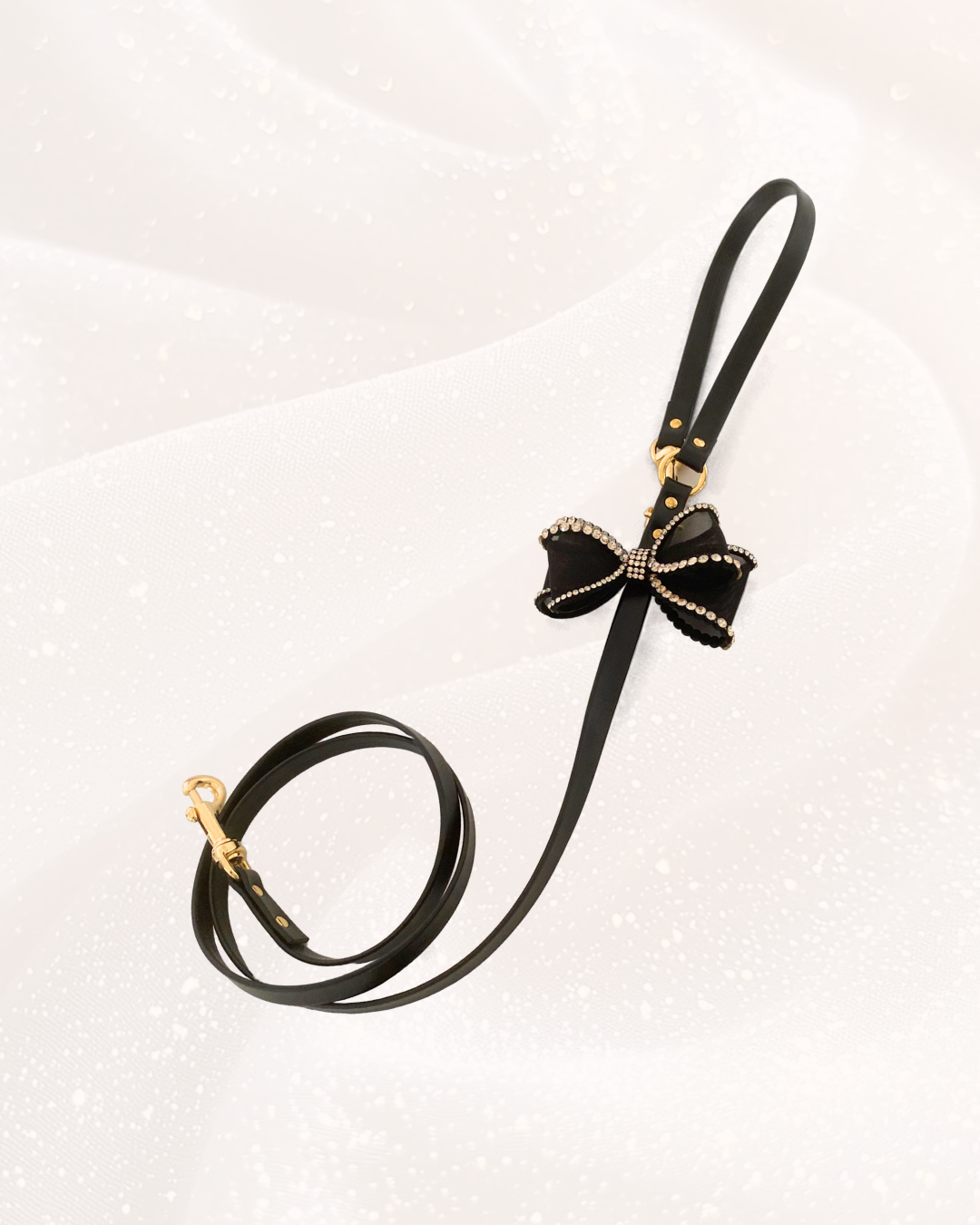 Guinzaglio gioiello nero con fiocco decorato da strass e dettagli dorati, disposto su sfondo bianco. 