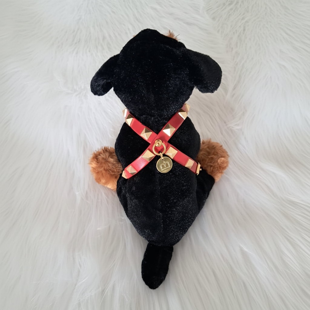 Cane in peluche con pettorina rossa con borchie e finiture oro visto dall'alto su una superficie in morbida ecopelliccia bianca – My Pets and I Milano